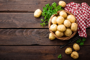 Raw potato in basket on wooden table, top view