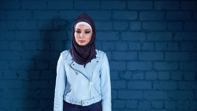 A portrait of a modern Muslim woman who wears a hijab and a leather jacket, a young woman with painted eyes looks into the camera. Arab woman is fashionably dressed