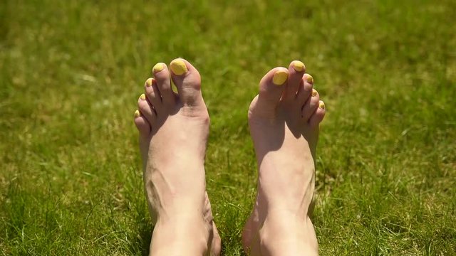 Female feet moving and posing on a sunlit green grass, close up.