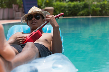 man with ukulele relaxing on the air mattress in the swimming pool