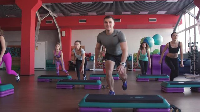 Step aerobics exercise class - group of people exercising on steppers with the trainer.