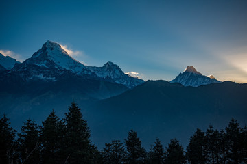 poonhill Winter sunset over snow-capped mountains with a view of the alpine valley and forest in the distance