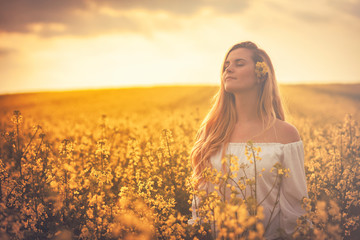 Smiling woman in yellow rapeseed field at sunset