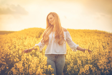 Smiling woman in yellow rapeseed field at sunset