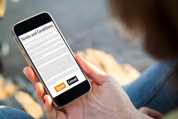 woman sitting in the street holding her smartphone reading terms and conditions
