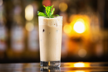 Closeup glass of coffee cocktail decorated with mint at bright bar counter background.