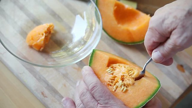 Scooping seeds from cantaloupe piece with a spoon