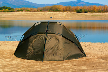 Landscape with fishing rods and hiking tent. Equipment for carp fishing with three fishing rods with reels on a support system - rod pod