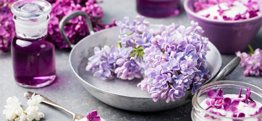 Obraz na płótnie Canvas Lilac flowers sugar and syrup, essential oil with flower blossoms in glass jar Grey stone background