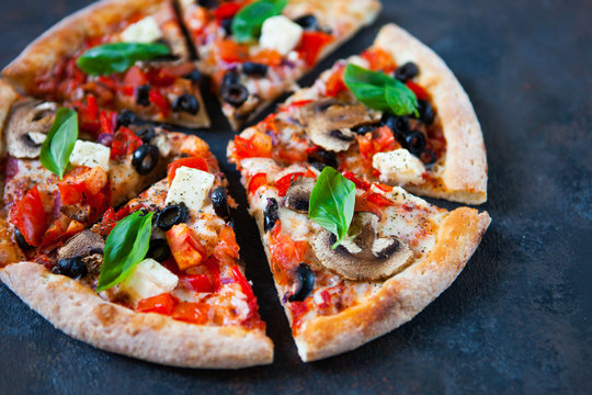 Hot testy pizza with tomatoes, mozzarella, mushrooms, olives, red pepper and basil on black concrete background. Copyspace. Top view.