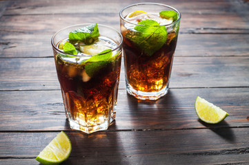 Homemade Cuba Libre with fresh lime, brown rum and crushed ice on an old wooden table