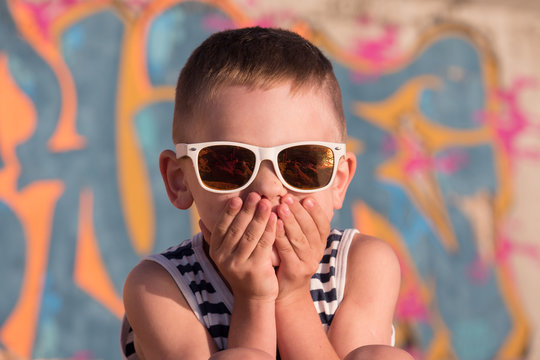 cool little boy wearing sunglasses closed his mouth with hands