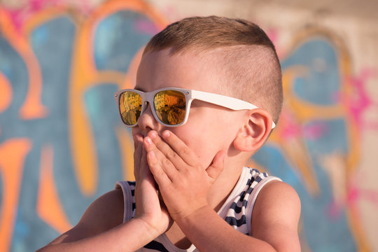 amazed little boy wearing sunglasses closed his mouth with hands
