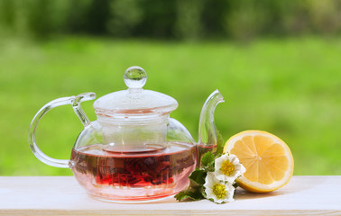 Teapot with fragrant herbal tea on a background of nature lemon and strawberry flower