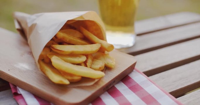 Packet of takeaway French fries or potato chips lying outdoors on a wooden picnic table for a tasty snack or as an accompaniment