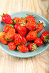 Ripe strawberry in a blue plate on a wooden background