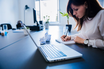 Portrait of businesswoman with laptop writes on a document at her office