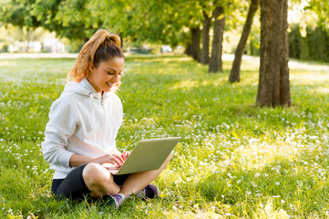 Young woman with laptop sitting on green grass in the park