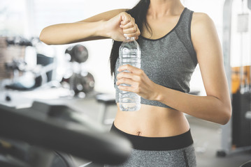 Asian woman in sportswear holding bottle of water at the gym.