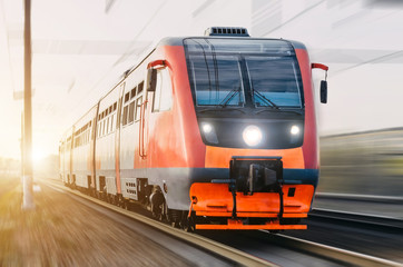 High-speed red passenger train rushing through the railway in the evening at sunset.
