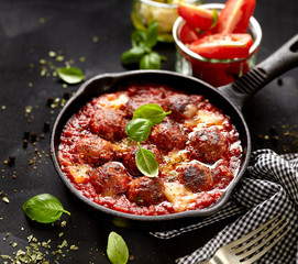 Meatballs in tomato sauce with addition cheese and fresh basil on iron pan, black background