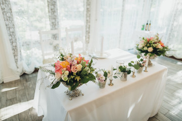 On the festive table in the wedding banquet area there are compositions of flowers, candles, plates, cutlery, napkins