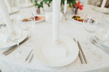 On the festive table in the wedding banquet area there are compositions of flowers, candles, plates, cutlery, napkins