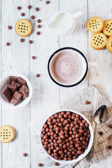 Hearty and tasty breakfast for children, cornflakes, chocolate balls with milk, cocoa and biscuits on a light wooden background 