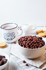 Hearty and tasty breakfast for children, cornflakes, chocolate balls with milk, cocoa and biscuits on a light wooden background 