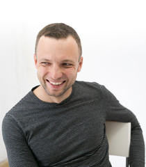 Fototapeta premium Young adult laughing man is sitting on a chair