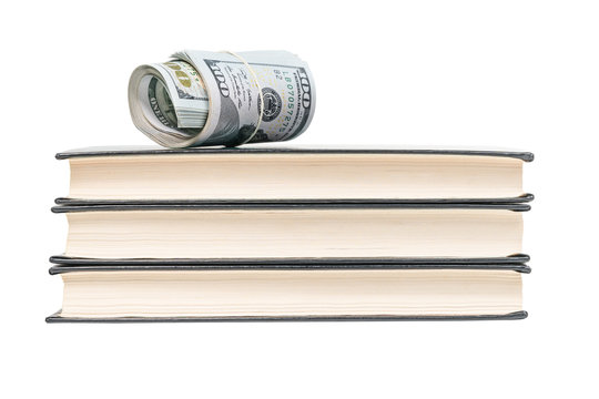 Money rolled into a tube and strapped a rubber band lying on top of a stack of three books