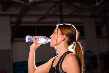 Fitness woman drinking water from bottle. Muscular young female at gym taking a break from workout.