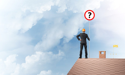 Businessman on brick house roof showing banner with question mark. Mixed media