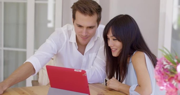 Happy young adult man and woman showing off ultrasound pictures of baby in womb to someone through a video chat on their tablet computer