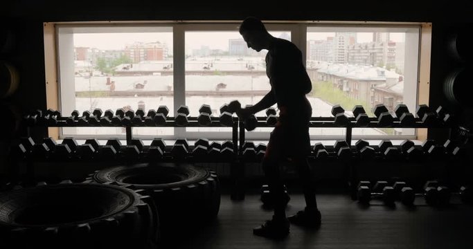 Silhouette of athletic man working out with dumbbells gym black background, man with dumbbells. Fitness.