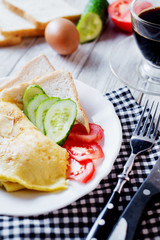 Hearty and tasty breakfast, traditional in the hotel, omelette from chicken eggs with cheese, fresh vegetables - cucumber and tomato, white toast and black coffee on a light wooden background