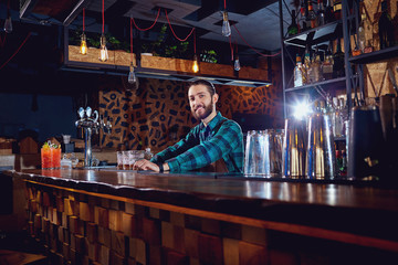 A barman with  beard behind counter in the bar.