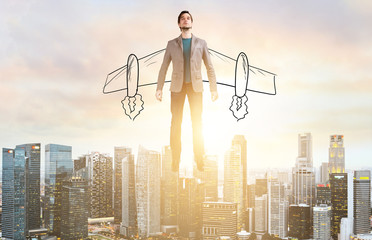 Business Advantage. Businessman with sketch wings hovering over down town on sunset.