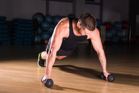Young Man Athlete Doing Pushups With Dumbbells As Part Of Bodybuilding Training.