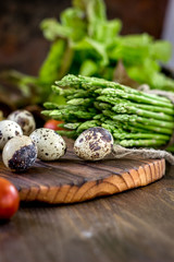Asparagus and quail eggs on wooden board.