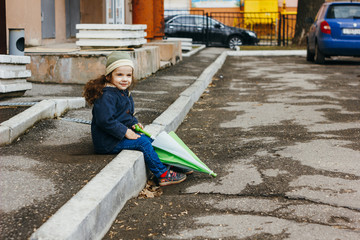 Little girl sitting with the umbrella on street.