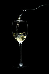 Wine is pouring from a bottle into a glass on a black background, studio light