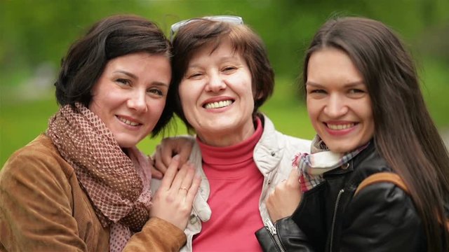 Two Smiling Sisters are Hugging and Kissing Their Mother Outdoors. Happy Family Spending Time Together in the Park.