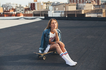 Young female in teenager millenial clothes rests on the rooftop on a sunny warm day in soft sunset...
