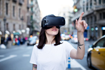 Beautiful young woman tries to understand if what she sees through the virtual glasses is real or just a projection, she gestures and points on things with her tattooed arm