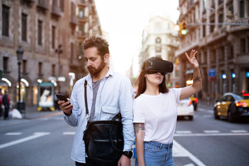 Handsome man and his girlfriend explore future world of immersive technology in the bust street with smartphone and VR googles