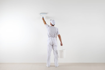 Rear view of painter man painting the wall, with paint roller and bucket, isolated on big empty space
