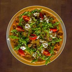 Delicious fresh pizza with mozzarella, cherry, arugula and parmesan on a wooden table. Top view.