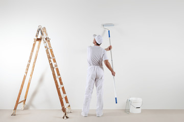 Rear view of painter man looking at blank wall, with paint stick roller, bucket and wooden ladder, isolated on white room