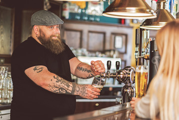 Cheerful bartender filling mug of cold lager in pub